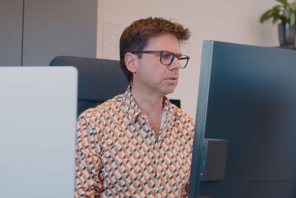 Mann mit Brille und gemustertem Hemd arbeitet am Computer in einem modernen Büro.