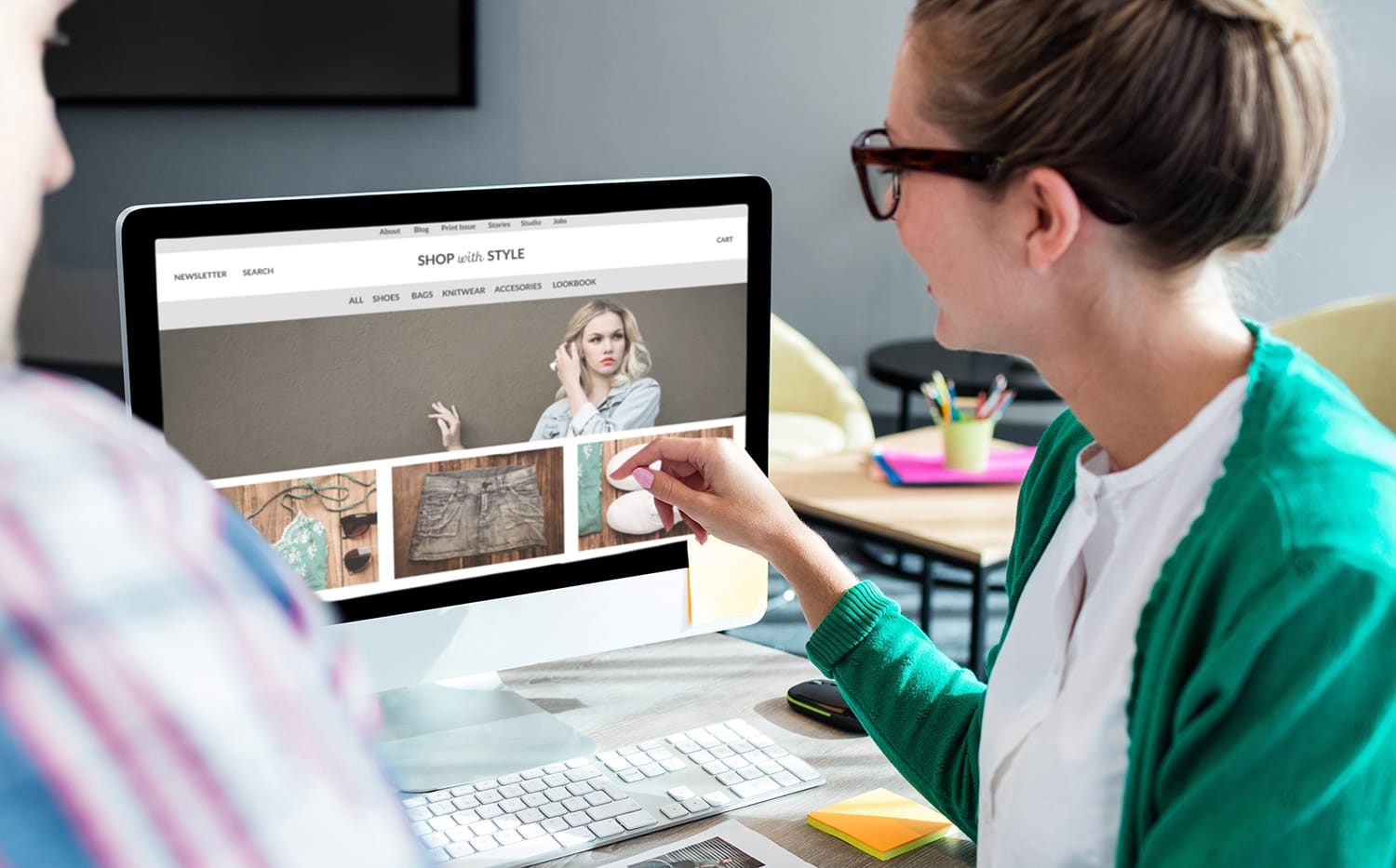 Zwei Personen an einem Schreibtisch schauen auf einen Computer, auf dem ein Online-Modegeschäft angezeigt wird.