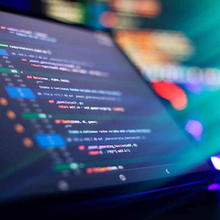 Nahaufnahme eines Computerbildschirms mit bunten Codezeilen und verschwommenen Lichtern dahinter.