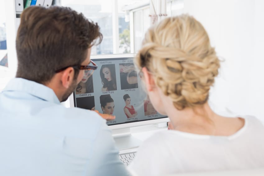 Zwei Personen sitzen an einem Schreibtisch und betrachten Kopfbilder auf einem Computerbildschirm. Gesichter nicht sichtbar.